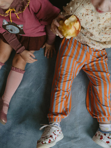 Two children in colorful outfits on a blue blanket, one eating an apple.