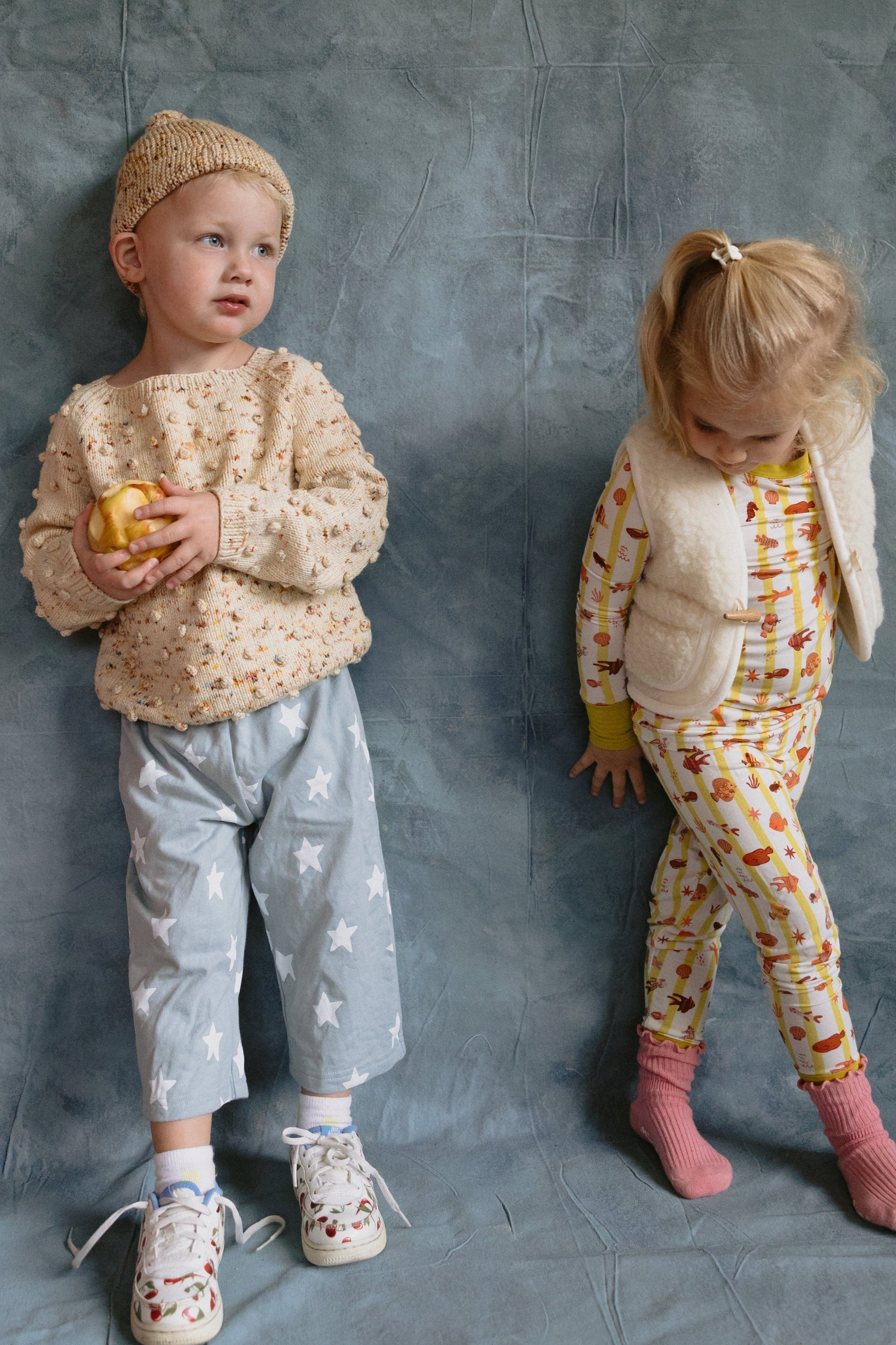 Two children in patterned outfits standing against a textured gray background