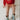 A child sitting on a white bed wearing a red crewneck sweatshirt with a colorful graphic print, a peach drawstring skirt, and light blue cowboy boots with gold trim.