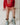 A child sitting on a white bed wearing a red crewneck sweatshirt with a colorful graphic print, a peach drawstring skirt, and light blue cowboy boots with gold trim.