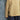A child standing against a textured blue-gray backdrop, wearing a pale yellow long-sleeve shirt with thin green horizontal stripes, navy pants with a small light pattern, and dark sneakers.