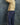 A young child standing in profile against a mottled blue-gray backdrop, wearing a yellow and cream striped long-sleeve top, navy pants with small white motifs and a paisley side panel, and purple sneakers.