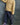 A child wearing a yellow and green striped long-sleeve shirt, navy blue pants with small white motifs and a paisley side stripe, and purple sneakers, standing against a textured blue backdrop.